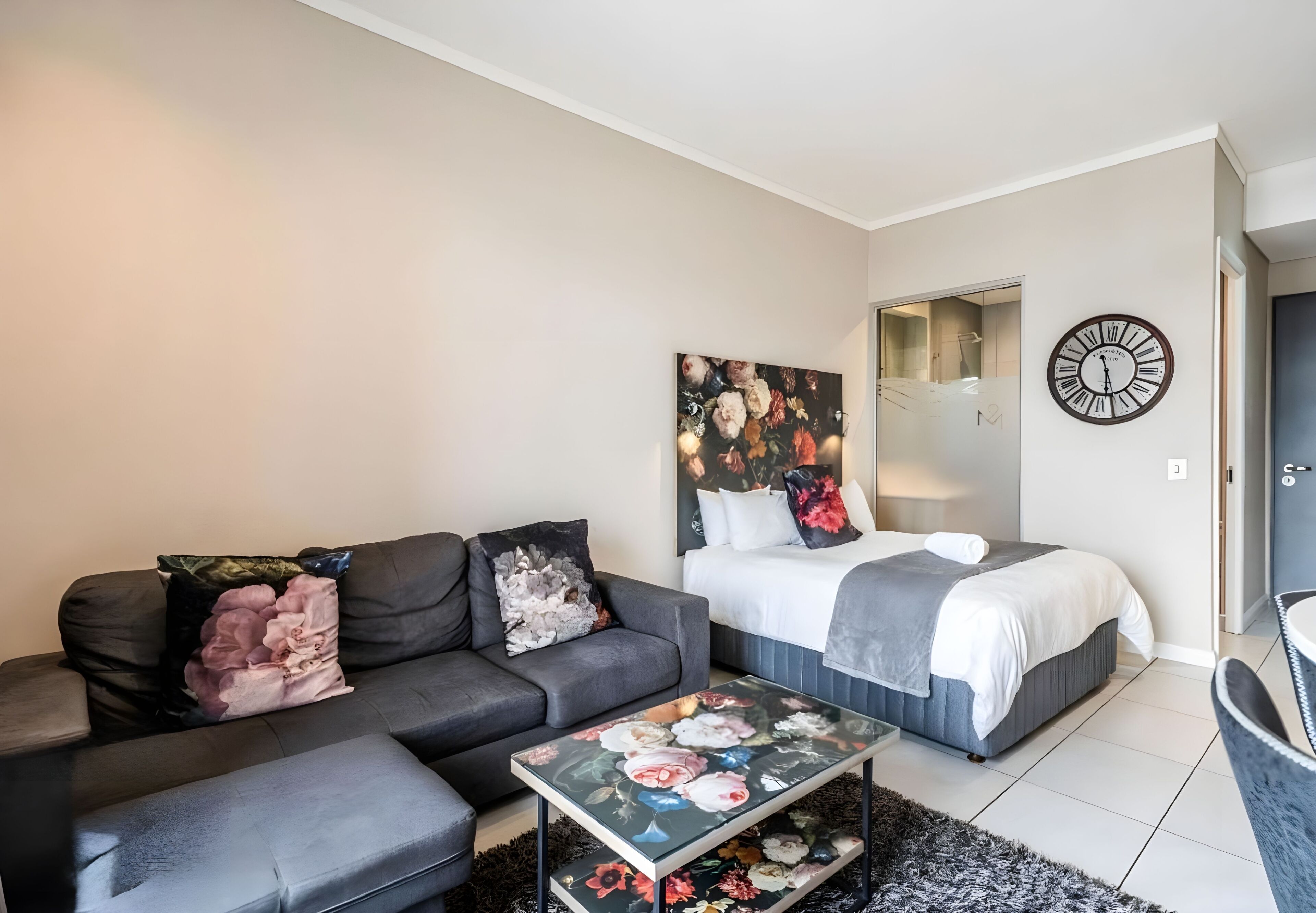 Quarto moderno com cama, sofá, mesa de centro e relógio de parede.