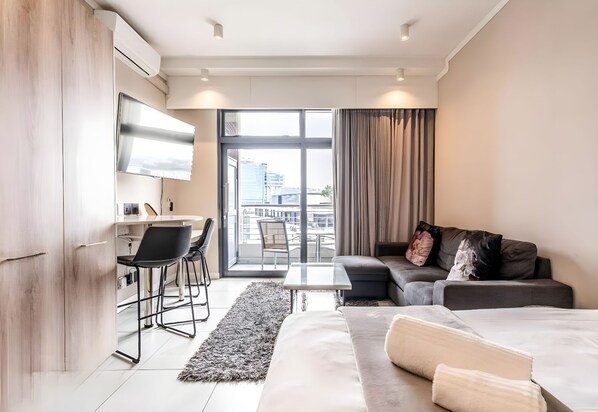 Ein modernes Hotelzimmer mit einer Couch, einem Bett, einem Schreibtisch mit Stühlen, einem Fernseher und Blick auf die Stadt.