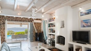Un salon avec un mur en pierre, une cheminée, un téléviseur et une vue sur l’extérieur.