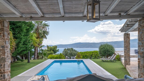 Une piscine avec vue sur la mer, entourée de verdure et de constructions en pierre.