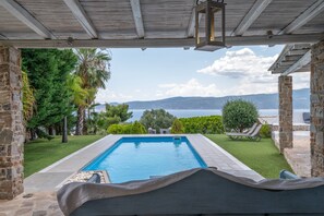 Una piscina con vista al mar, rodeada de vegetación y estructuras de piedra.