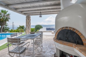 Un patio al aire libre con una mesa y sillas de piedra, un horno de ladrillo y una piscina.