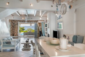 Una cuina moderna amb una paret de pedra, una zona de dinar amb mobiliari blanc i vista a l'exterior.