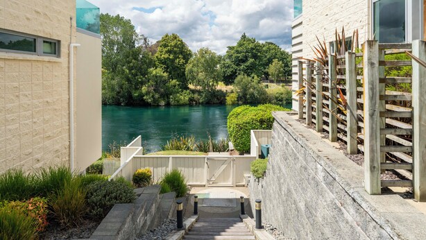 A stone staircase leading to a gated entrance with a view of a lake and surrounding greenery. - Riverlight Nook - Lake Taupo Holiday Home (Taupo)
