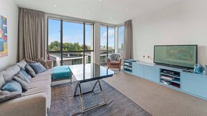 A modern living room with a sofa, a glass coffee table, a TV, and a view of the outdoors. - Riverlight Nook - Lake Taupo Holiday Home (Taupo)