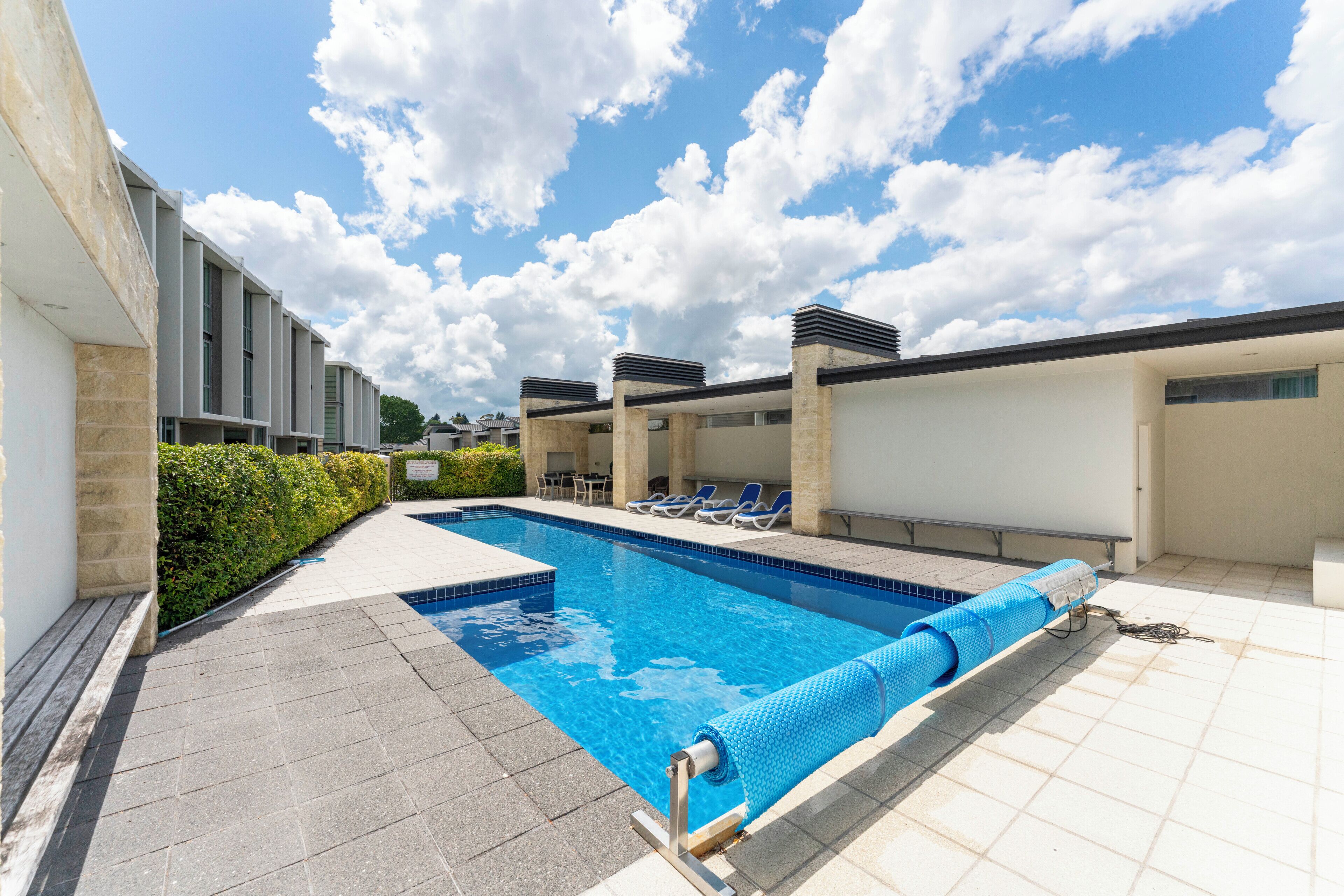 Ein Schwimmbecken mit Liegestühlen, einer gefliesten Terrasse und blauem Himmel.