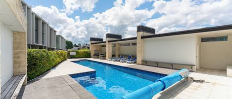 Ein Schwimmbecken mit Liegestühlen, einer gefliesten Terrasse und blauem Himmel.