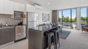 A modern kitchen with stainless steel appliances, a central island with bar stools, and a large window offering a city view. - Riverlight Nook - Lake Taupo Holiday Home (Taupo)