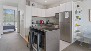 A modern kitchen with white cabinets, stainless steel appliances, and a central island with bar stools. - Riverlight Nook - Lake Taupo Holiday Home (Taupo)