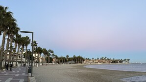 A beach with palm trees, a paved walkway, and buildings in the background. - Casa Anna - Velapi II - Los Alcázares (San Javier)