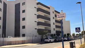 A multi-story building with balconies, a pedestrian crossing sign, and a street with parked cars. - Casa Anna - Velapi II - Los Alcázares (San Javier)