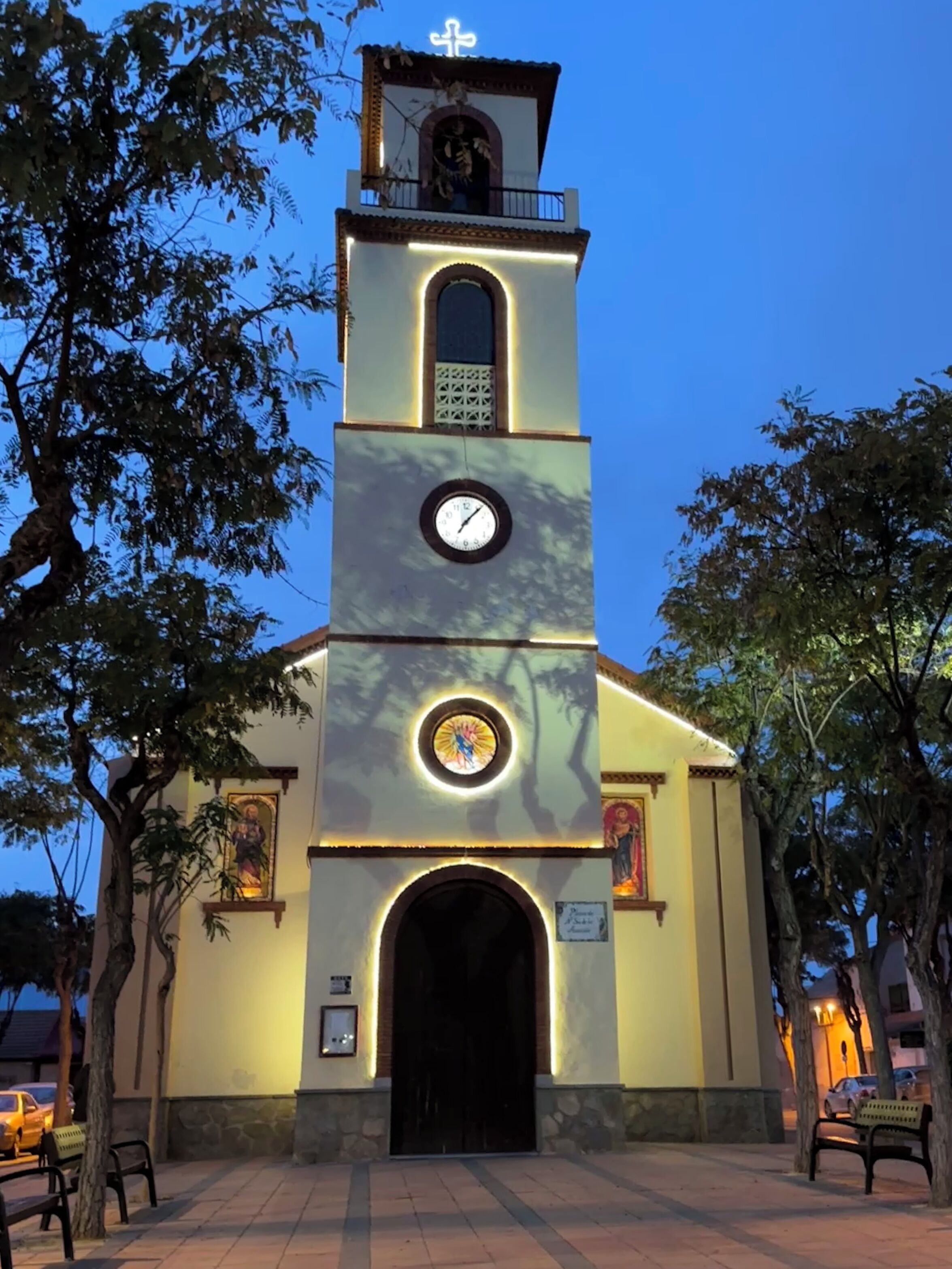 Una iglesia con una torre del reloj, una entrada en arco y una cruz en la parte superior.
