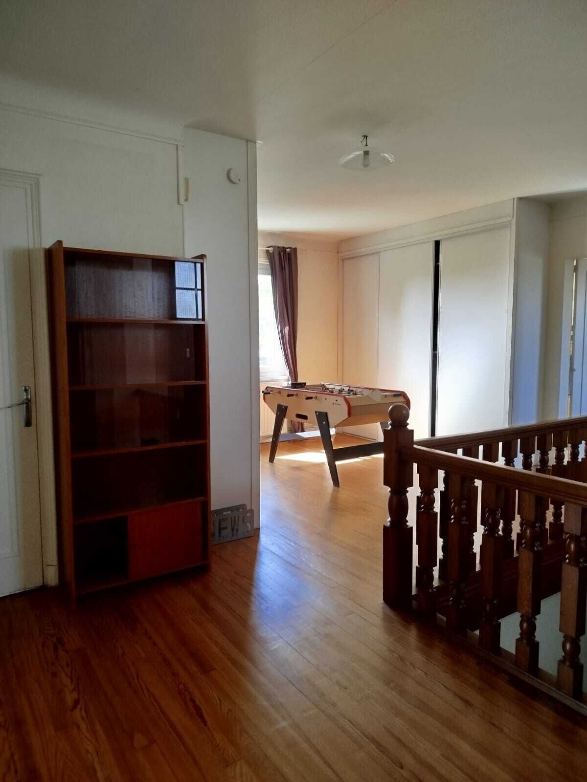 A room with a wooden floor, a bookshelf, a foosball table, and a staircase.
