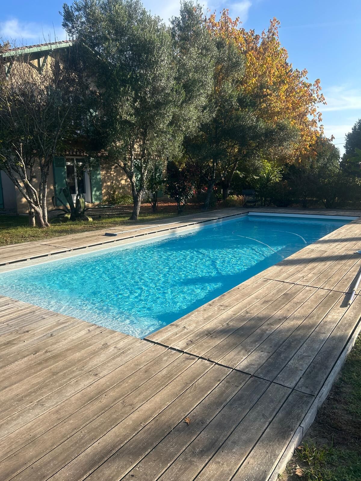Ein rechteckiger Swimmingpool mit klarem, blauem Wasser, umgeben von einer Holzterrasse.