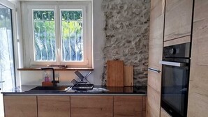 Eine moderne Küche mit Holzschränken, einer Wand mit Steinverkleidung, einem Einbauofen und einem Fenster mit Blick auf Bäume.