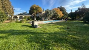 Ein Garten mit Schwimmbecken, einer überdachten Terrasse und einem Gebäude mit Bogenfenstern.
