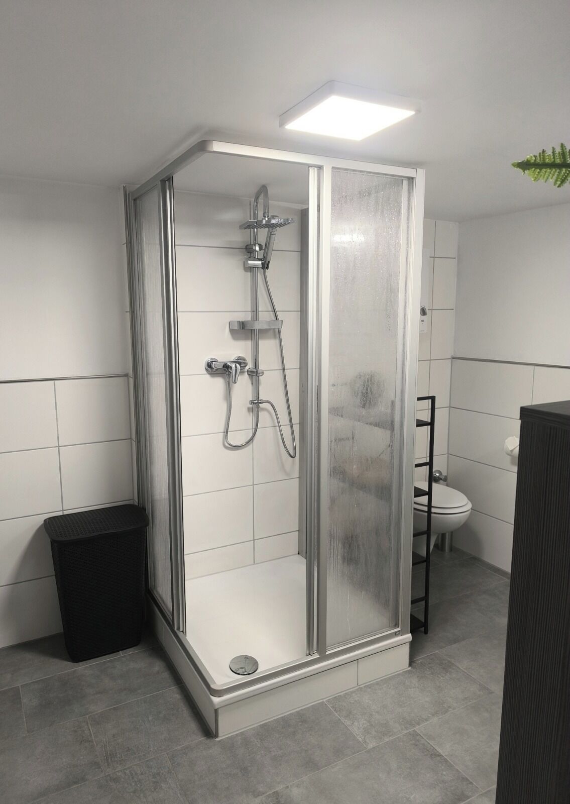 Une douche fermée par des parois en verre, dotée d’un pommeau de douche à main et d’un robinet fixé au mur.