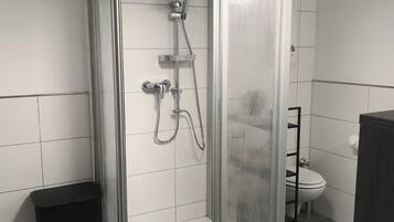 Une douche fermée par des parois en verre, dotée d’un pommeau de douche à main et d’un robinet fixé au mur.