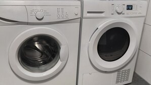 Two front-loading washing machines in a modern bathroom with white tiles and a potted orchid. - Top location! Modern 2-room apartment (Aschaffenburg)