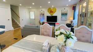 Uma sala de estar moderna com sofá, mesa de jantar com cadeiras, televisão e objetos decorativos.