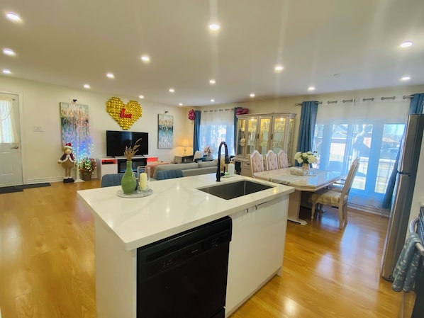 A modern kitchen with a dishwasher, a dining area with a table and chairs, a sofa, and a TV.