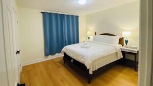 Quarto com uma cama, duas mesas de cabeceira com luminárias, uma janela com cortinas azuis e assoalho de madeira.