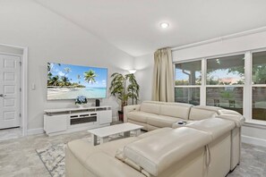 Una sala de estar moderna con un sofá modular, un televisor de pantalla plana, una planta en maceta y ventanas amplias.