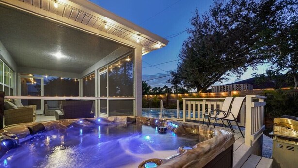 A hot tub with a glass enclosure, outdoor seating, and a barbecue grill.