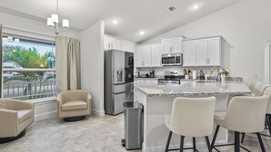 A modern kitchen with white cabinets, stainless steel appliances, a granite countertop island, and a bar stool seating area.