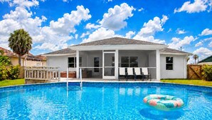 A swimming pool with a lounge area, a covered patio, and a view of the sky.