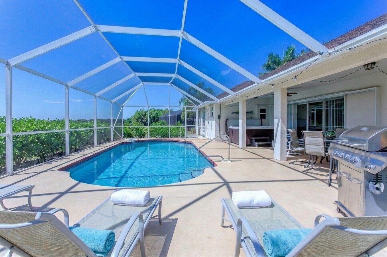 A covered outdoor swimming pool with lounge chairs, a barbecue grill, and a patio area.