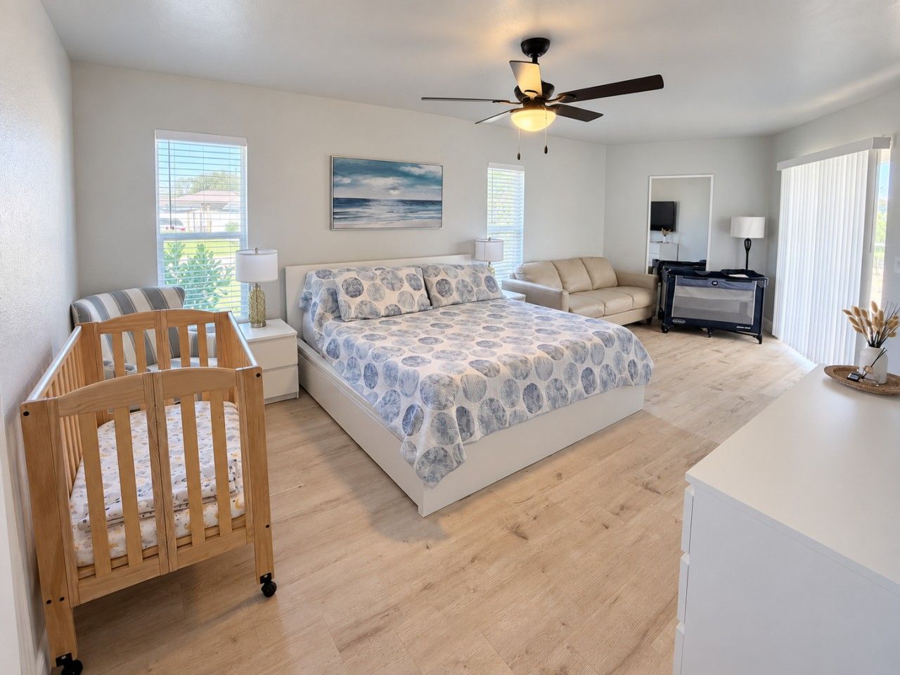 A bedroom with a bed, a crib, a desk, and a ceiling fan.