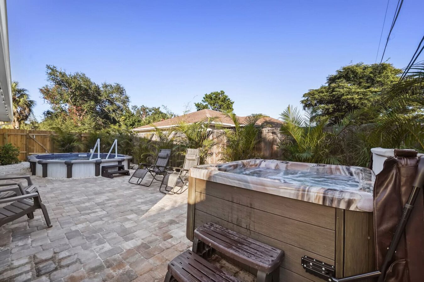 An outdoor patio with a hot tub, lounge chairs, and a wooden bench.