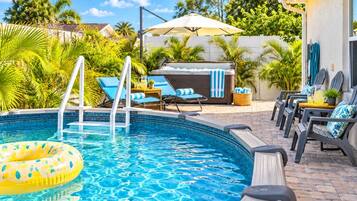 A swimming pool with a hot tub, lounge chairs, and a covered patio area.