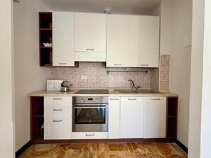 Eine kleine Küche mit weißen Schränken, einem eingebauten Backofen, einer Spüle aus Edelstahl und einer gefliesten Rückwand.