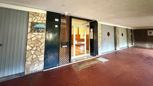 Um corredor com parede de pedra, uma porta com a inscrição 'PUBLICA' e um aviso com o símbolo de proibido fumar.