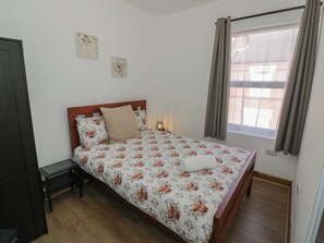 A bedroom with a wooden bed, floral bedding, a bedside table, a nightstand, and a window with curtains. - JMG House (West Bromwich)