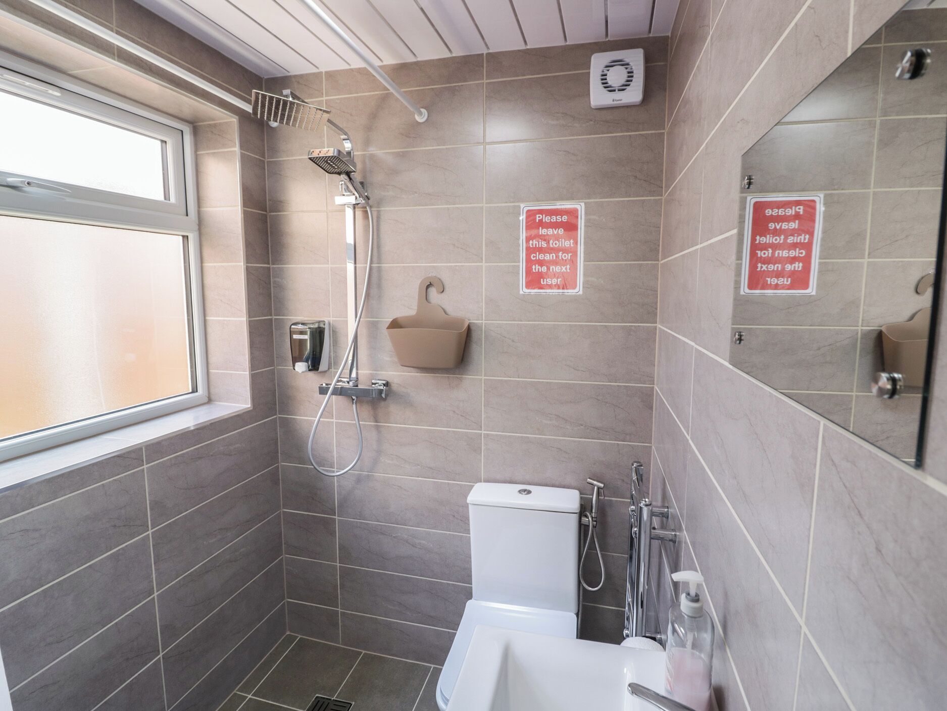A bathroom with a shower, toilet, and sink. There are signs instructing to leave the toilet clean for the next user.