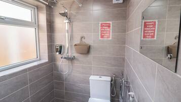 A bathroom with a shower, toilet, and sink. There are signs instructing to leave the toilet clean for the next user.