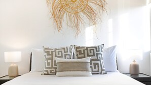 Een net opgemaakt bed met patroon kussens, een decoratieve wandhanger en bedlampjes.