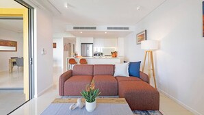 Een moderne woonkamer met een bank, een eethoek en een keuken op de achtergrond.