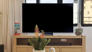 Een televisie op een houten standaard, een kamerplant en een vaas met planten op een tafel.