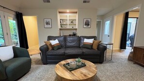 Ein Wohnzimmer mit einem dunkelbraunen Ledersofa, einem runden Holztisch und einem Bücherregal.