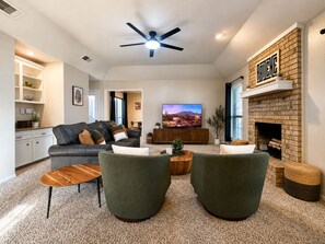 A modern living room with a fireplace, a television, and a ceiling fan. - Abilene Urban Oasis-Modern/Sleeps 8/Games/Walk to ACU/Gorgeous Backyard (Abilene)