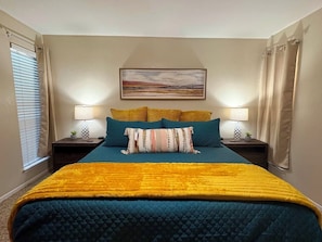 Un dormitorio con cama, dos mesitas de noche, un cuadro y una ventana con cortinas.