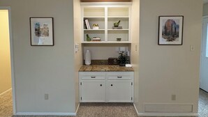 A compact kitchen with white cabinetry, a granite countertop, and a built-in shelving unit.