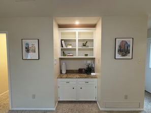A compact kitchen with white cabinetry, a granite countertop, and a built-in shelving unit.