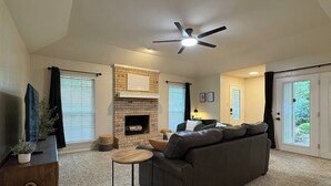 Ein Wohnzimmer mit Kamin, einer Couch, einem Fernseher und einem Deckenventilator.