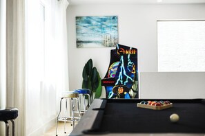 Ein Billardtisch mit Spielball, eine Billardtasche mit Grafik, ein Barhocker und eine Pflanze.