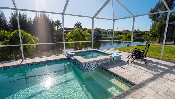 En pool med klart vand, omgivet af en overdækket patio med en stol og et lille bord.